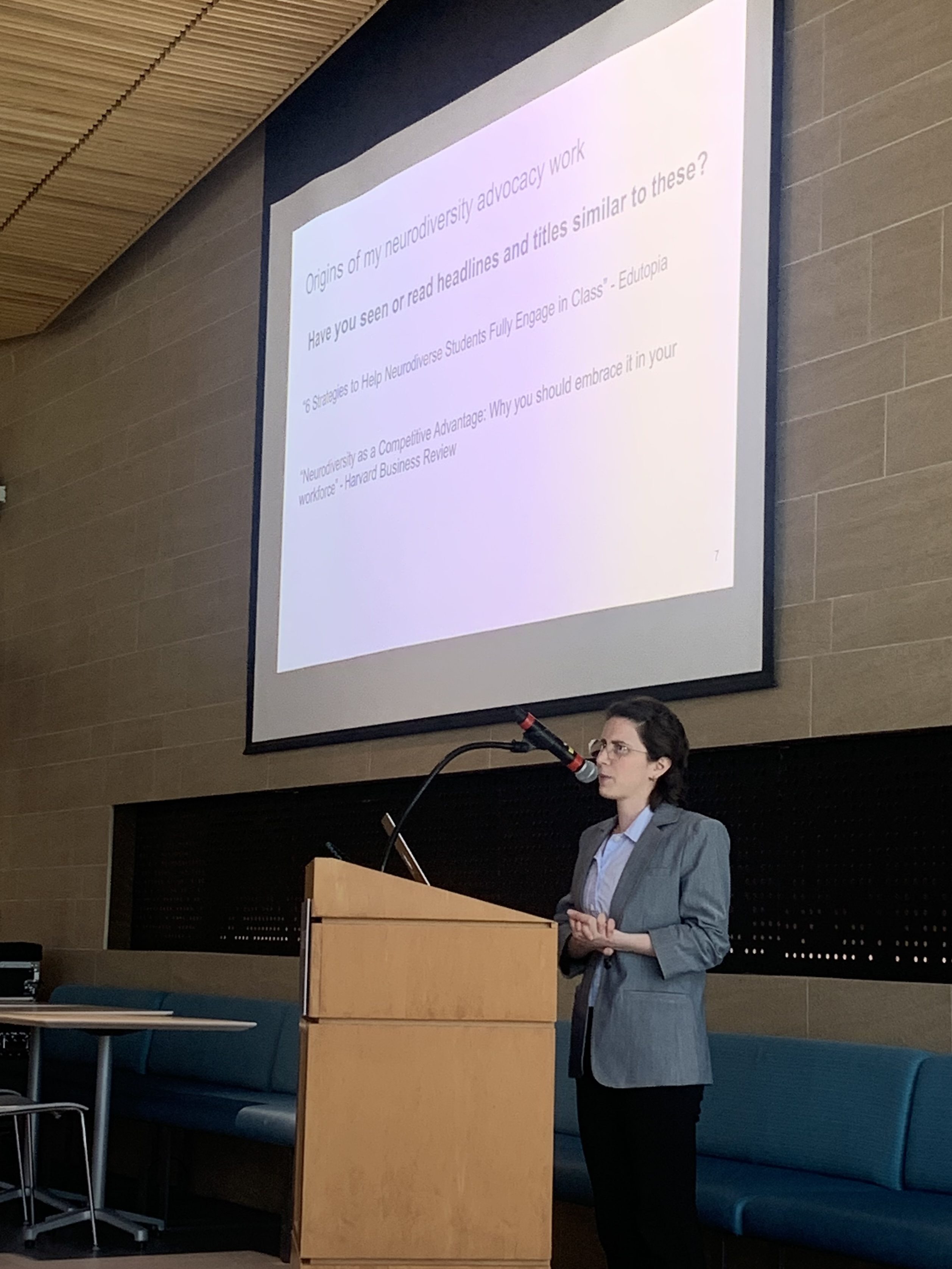 Sarah Silverman (short white woman wearing a blue jacket) standing at a podium in front of a projection screen.